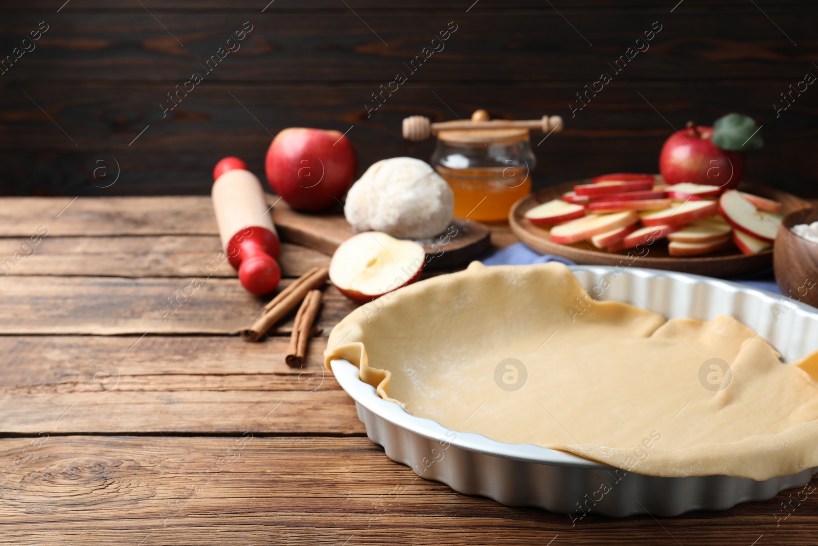 Photo of Raw dough and ingredients on wooden table, space for text. Baking apple pie