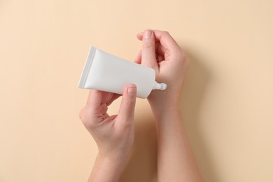 Woman applying cosmetic cream from tube onto her hand on beige background, top view