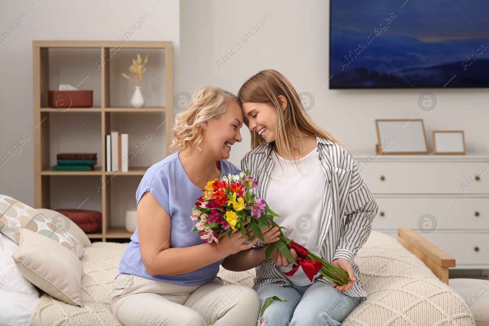 Photo of Young daughter congratulating her mom with flowers at home. Happy Mother's Day