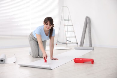 Photo of Woman applying glue onto wallpaper sheet in room