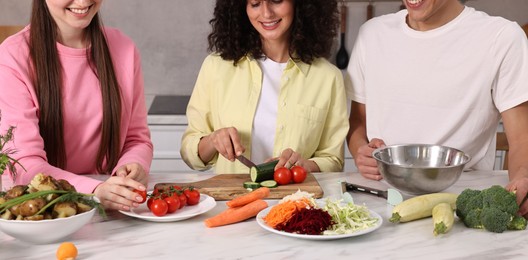 Friends cooking healthy vegetarian meal at white marble table in kitchen, closeup