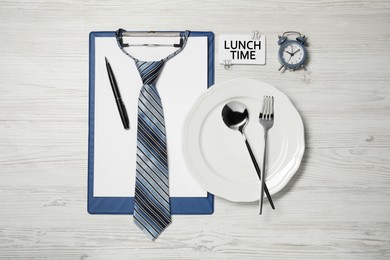 Image of Creative business lunch layout. Clipboard, tie, plate, cutlery, card and alarm clock on white wooden table, flat lay