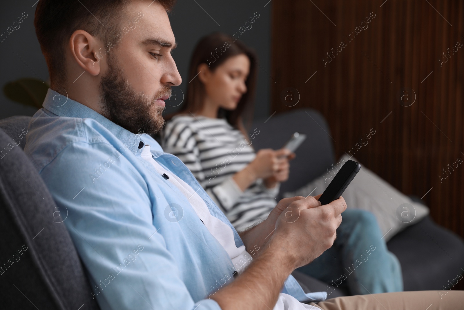 Photo of Couple addicted to smartphones ignoring each other at home. Relationship problems
