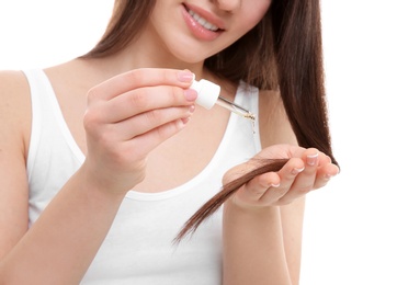 Photo of Young woman applying oil onto hair on white background