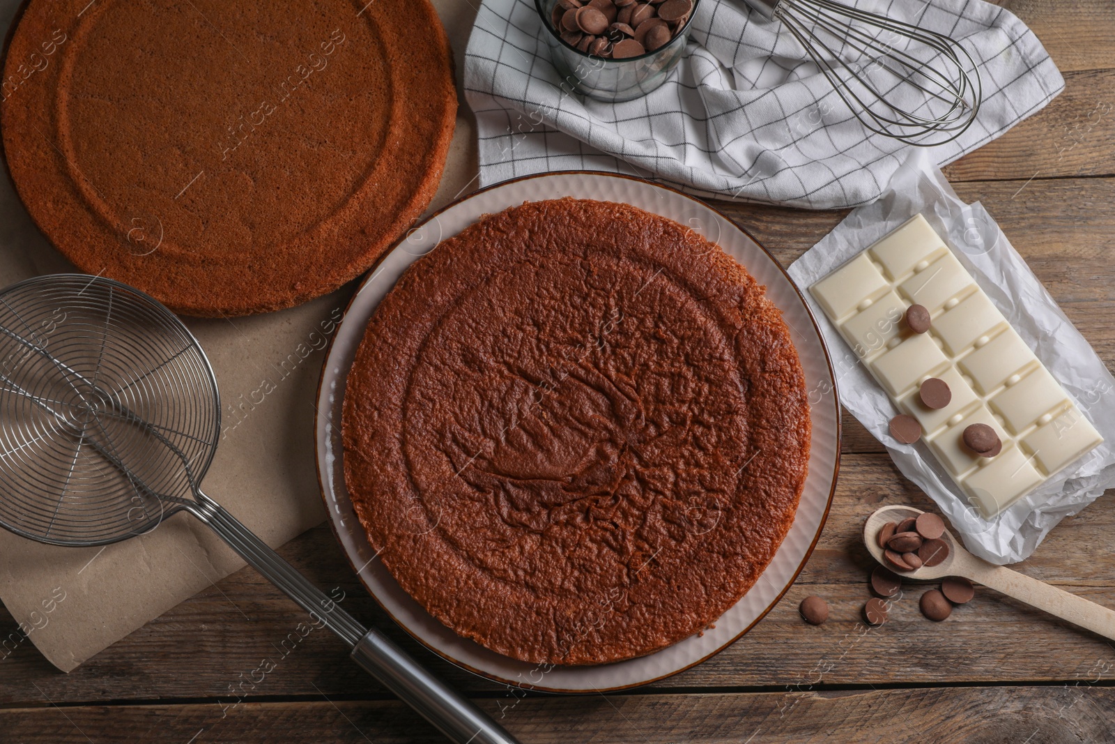 Photo of Delicious homemade sponge cake and different kinds of chocolate on wooden table, flat lay