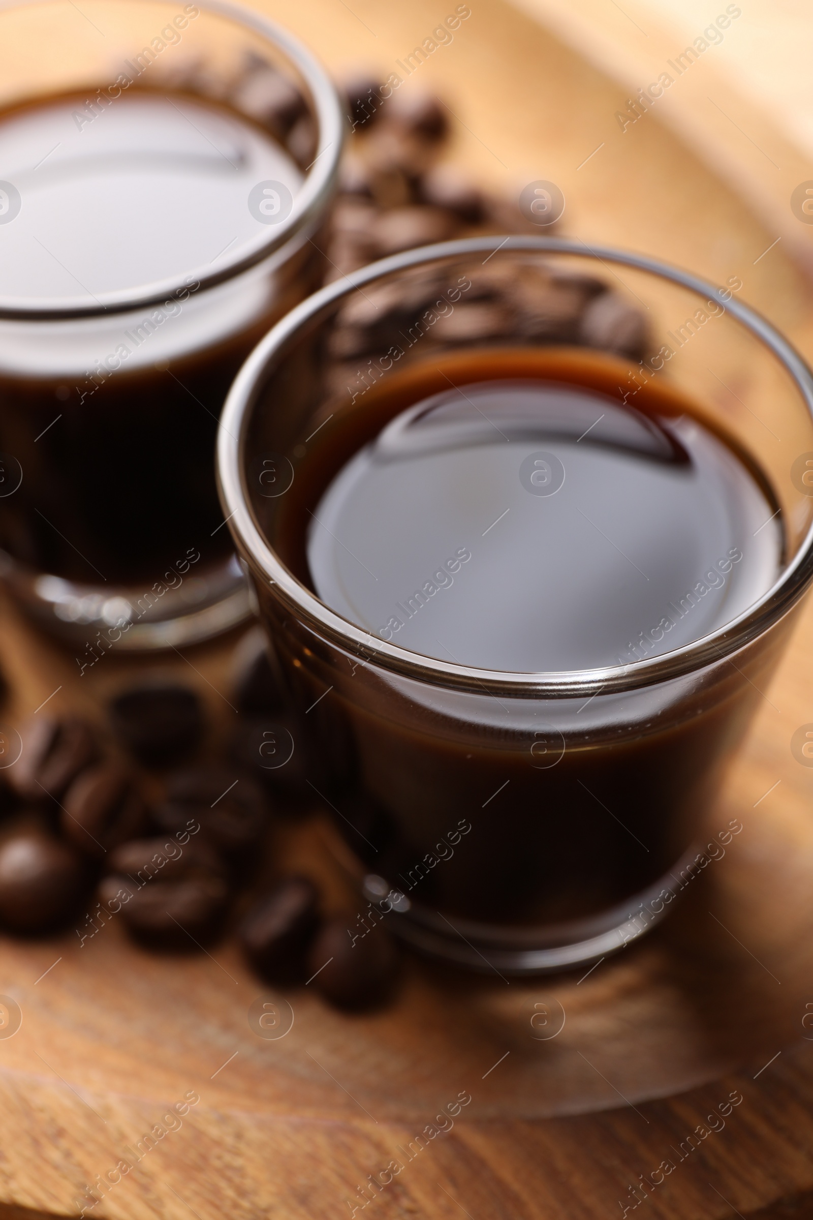 Photo of Shot glasses with coffee liqueur and beans on wooden tray, closeup