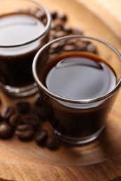 Photo of Shot glasses with coffee liqueur and beans on wooden tray, closeup