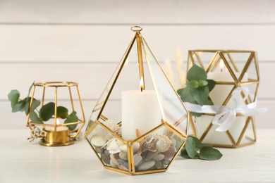Photo of Stylish glass holders with burning candles and beautiful decor on white wooden table