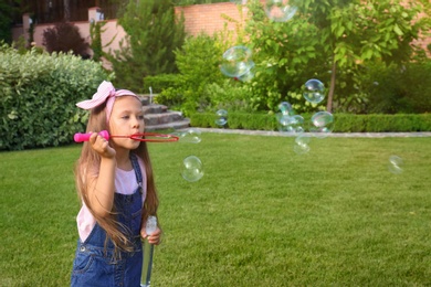Photo of Cute little girl blowing soap bubbles in green park
