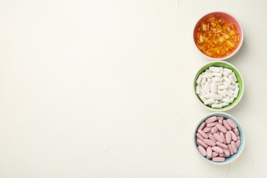 Photo of Different vitamin capsules in bowls on white wooden table, flat lay. Space for text
