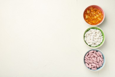 Different vitamin capsules in bowls on white wooden table, flat lay. Space for text