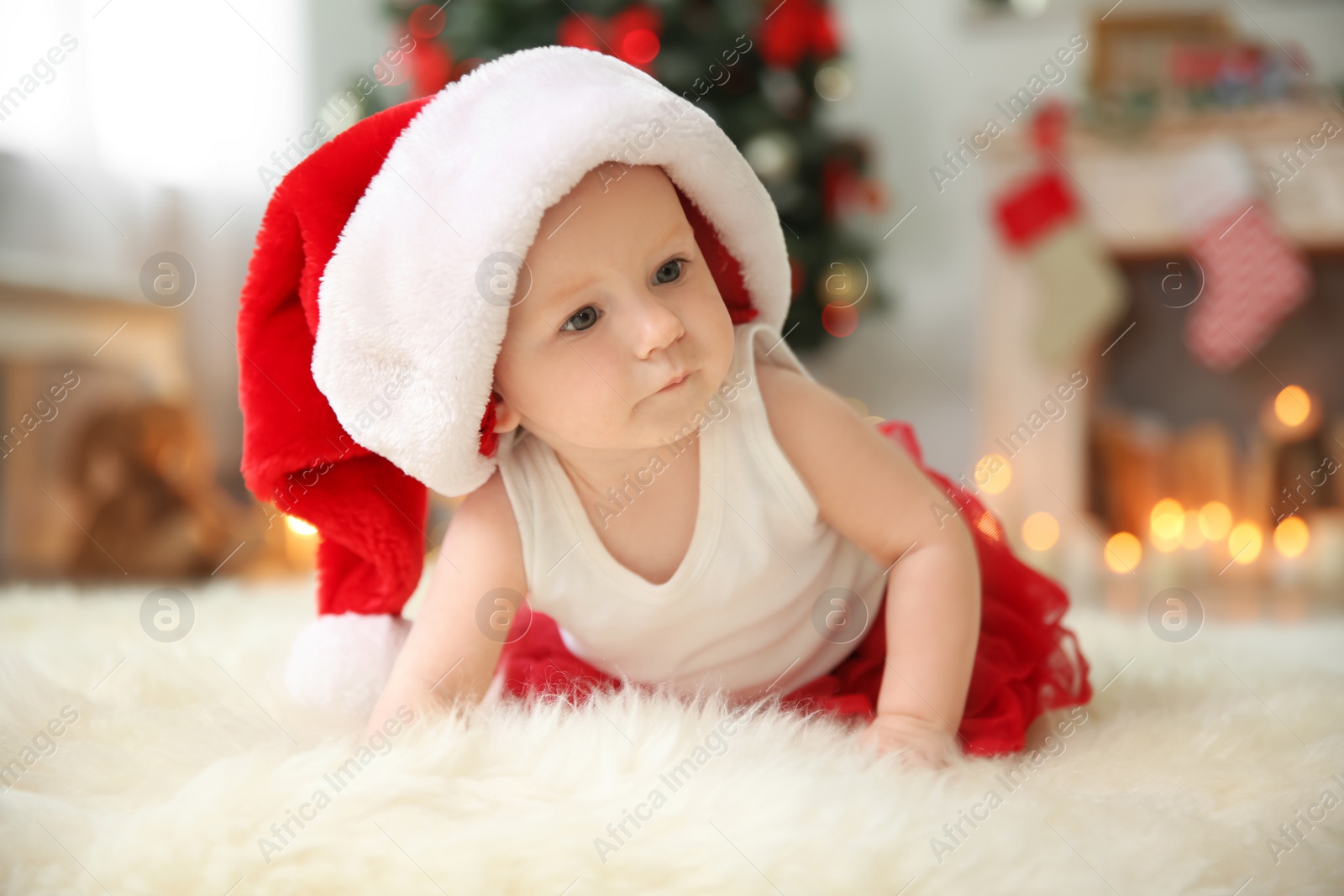 Photo of Cute baby in Santa hat on floor at home. Christmas celebration