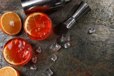 Photo of Aperol spritz cocktail, ice cubes and orange slices in glasses and shaker on grey textured table, flat lay. Space for text