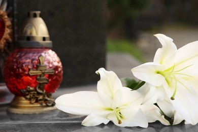 Photo of White lilies and grave light on grey granite tombstone outdoors, closeup. Funeral ceremony