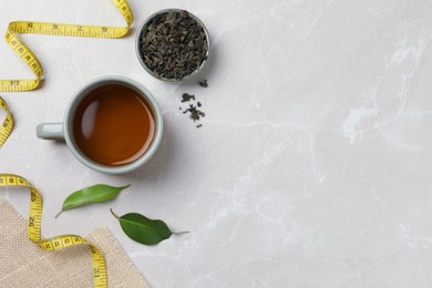 Flat lay composition with herbal diet tea and measuring tape on light marble table, space for text. Weight loss concept