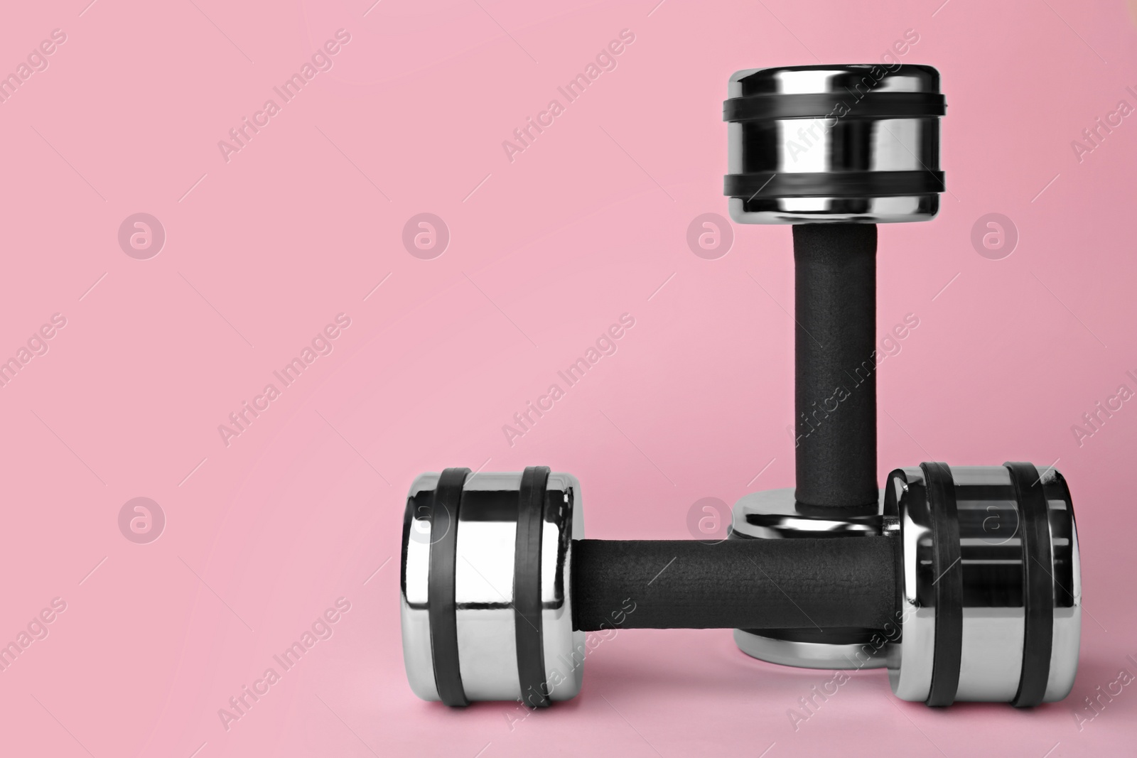 Photo of Two metal dumbbells on light pink background