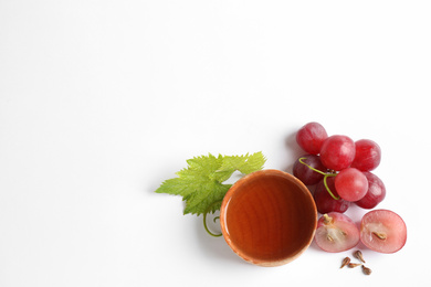 Organic red grapes, seeds and bowl of natural essential oil on white background, flat lay. Space for text