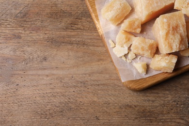 Photo of Pieces of delicious parmesan cheese on wooden table, top view. Space for text