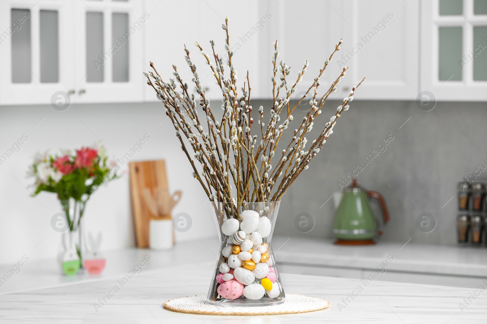 Photo of Vase with beautiful pussy willow branches and painted eggs on table in kitchen. Easter decor