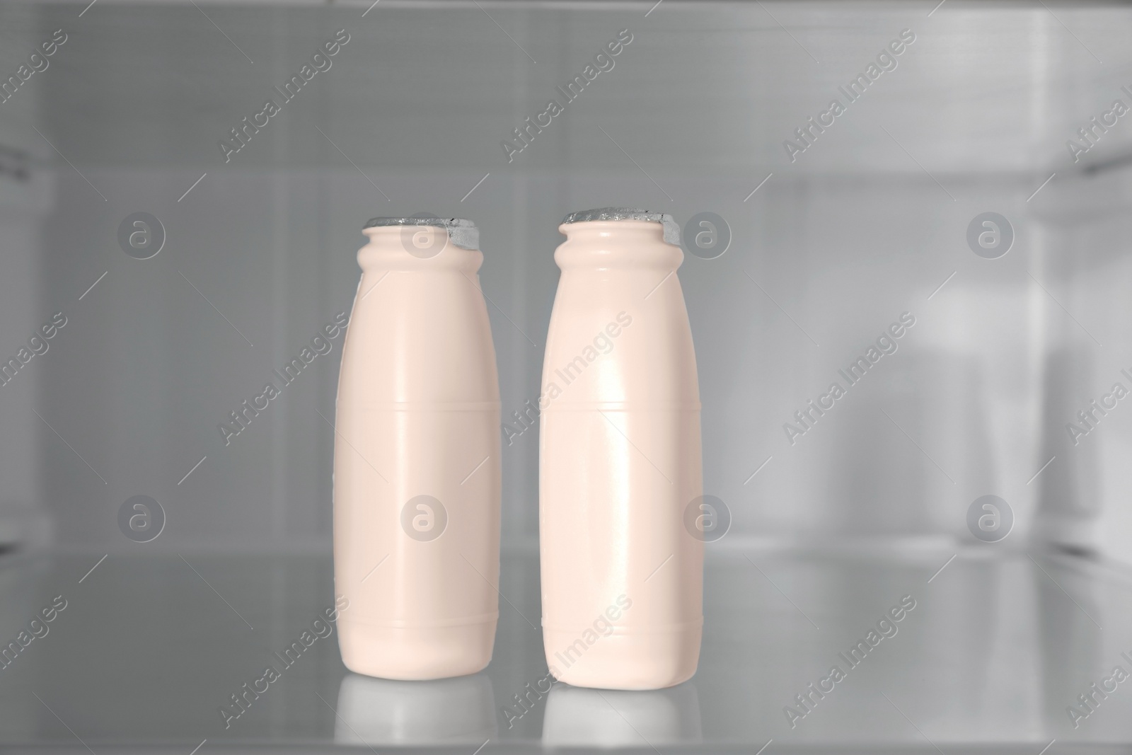 Photo of Bottles of yogurt on shelf inside modern refrigerator, closeup