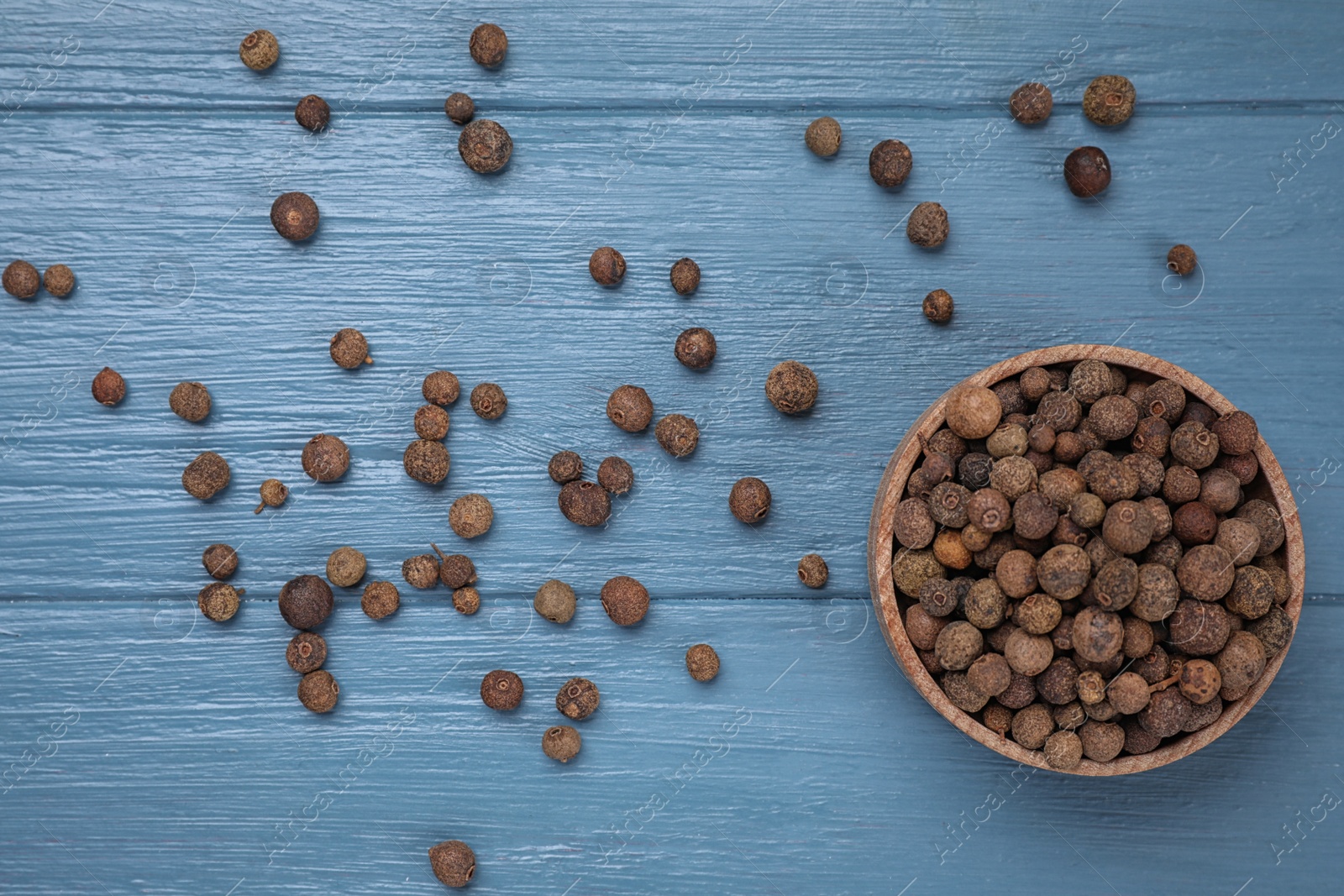 Photo of Black peppercorns in bowl on blue wooden table, flat lay