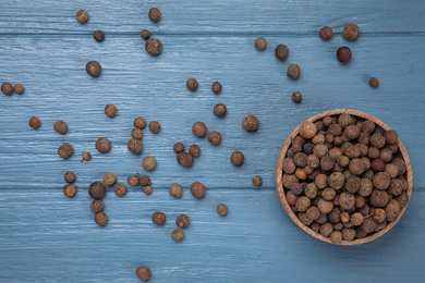 Black peppercorns in bowl on blue wooden table, flat lay