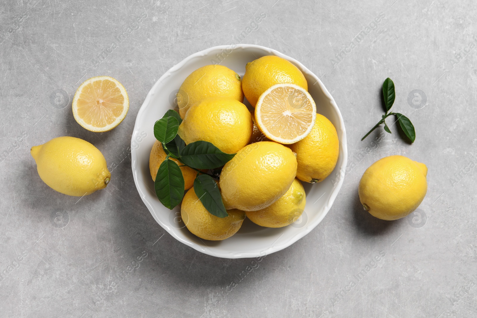 Photo of Fresh lemons and green leaves on grey table, top view