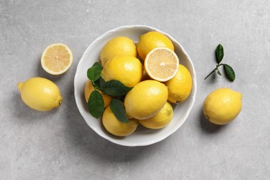 Fresh lemons and green leaves on grey table, top view