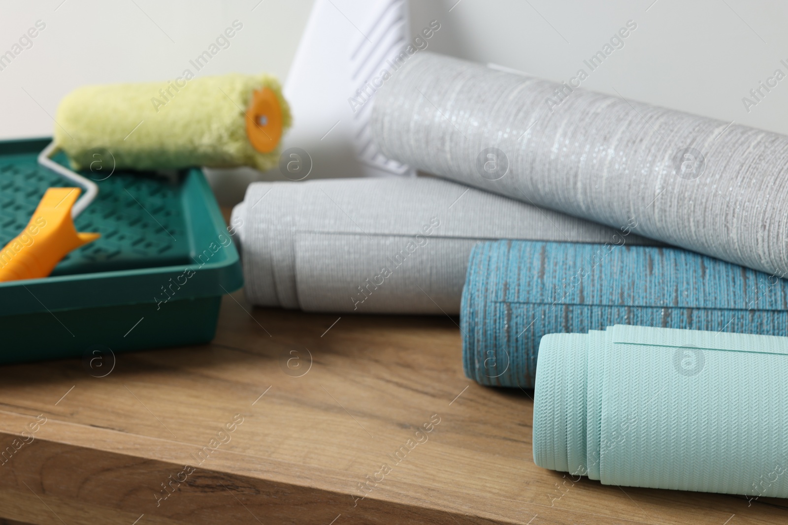 Photo of Different wallpaper rolls, roller and plastic spatula on wooden table