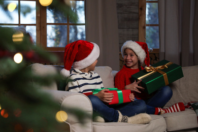 Happy children wearing Santa hats with Christmas gifts on sofa at home