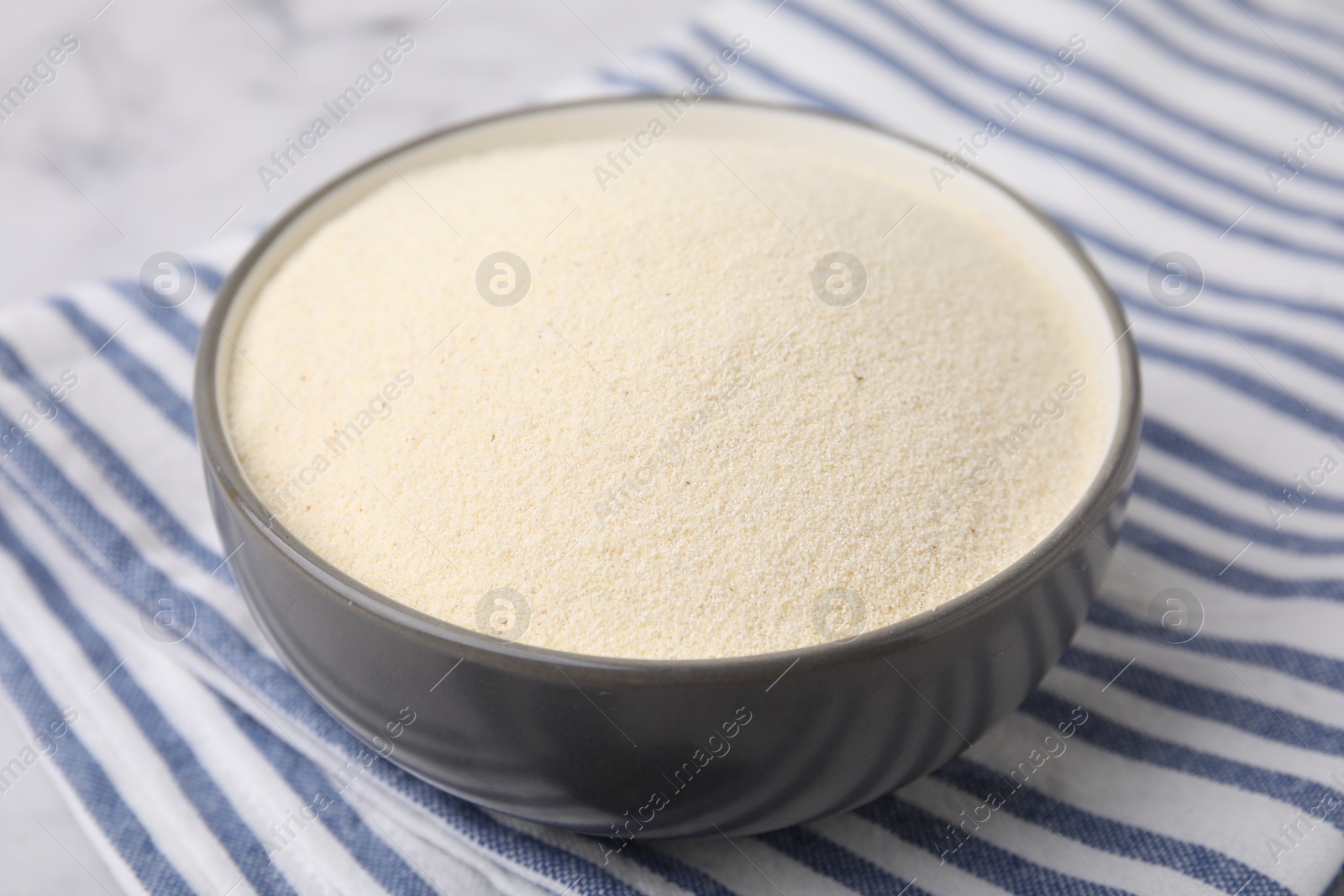 Photo of Bowl of uncooked organic semolina on white marble table, closeup