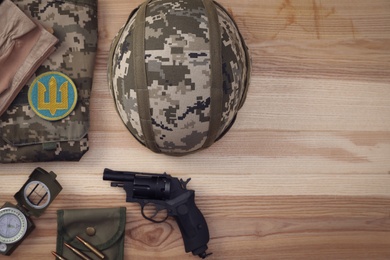 Photo of MYKOLAIV, UKRAINE - SEPTEMBER 26, 2020: Tactical gear, military uniform and Ukrainian army patch on wooden table, flat lay. Space for text