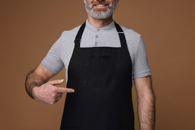 Photo of Man pointing at kitchen apron on brown background, closeup. Mockup for design