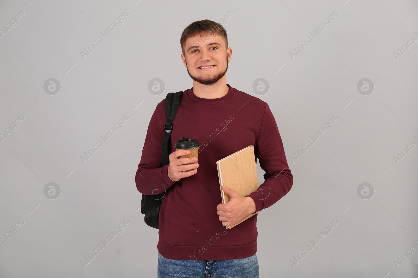 Photo of Young student with backpack, book and cup of coffee on grey background