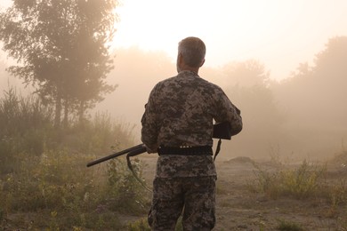 Photo of Man with hunting rifle wearing camouflage outdoors, back view