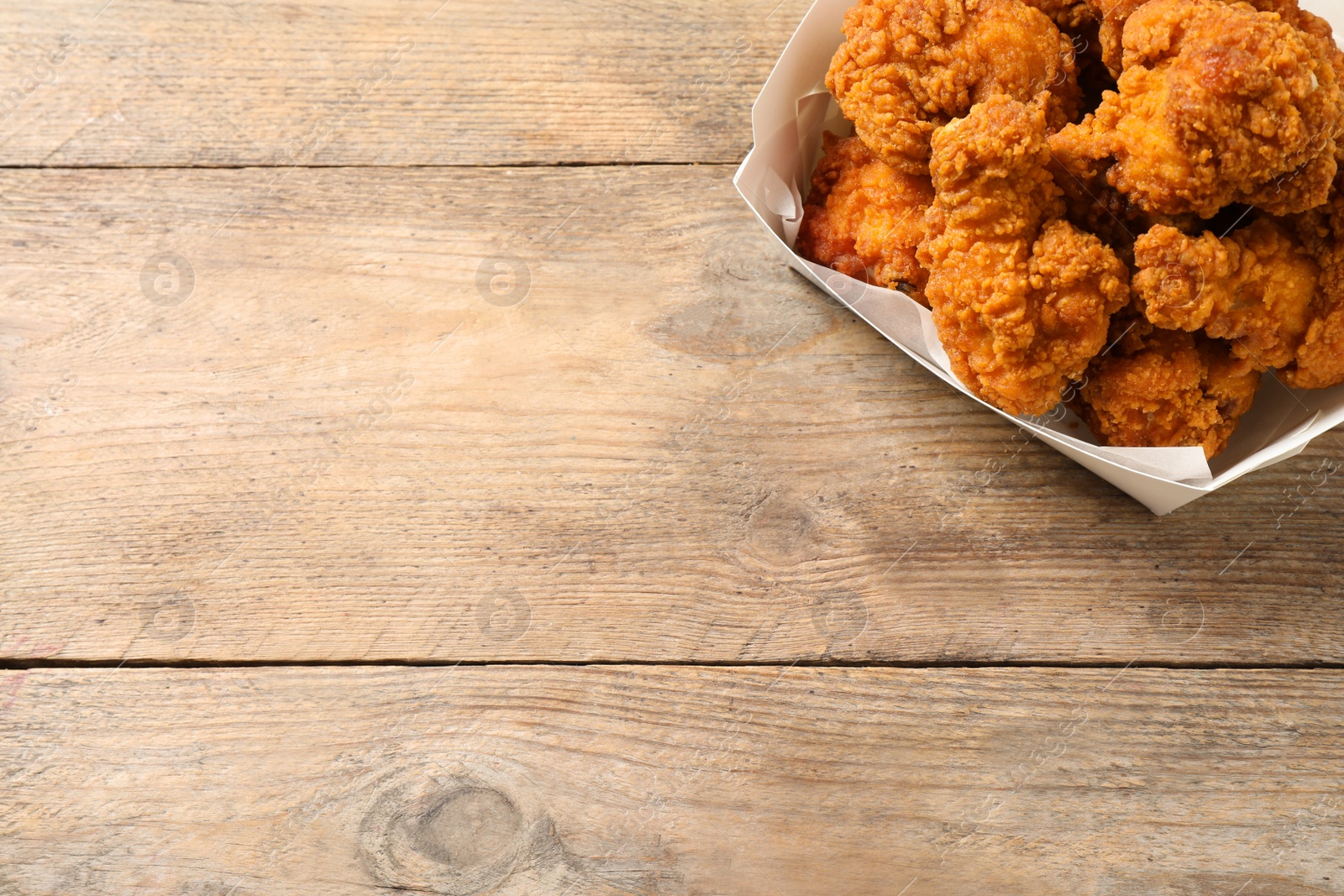 Photo of Tasty deep fried chicken pieces on wooden table, top view. Space for text