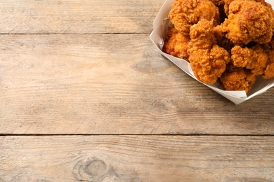 Tasty deep fried chicken pieces on wooden table, top view. Space for text