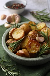 Tasty baked potato and aromatic rosemary in bowl on table, closeup