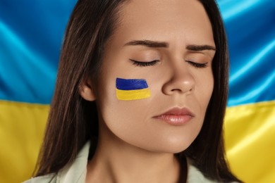 Photo of Sad young woman with face paint near Ukrainian flag, closeup