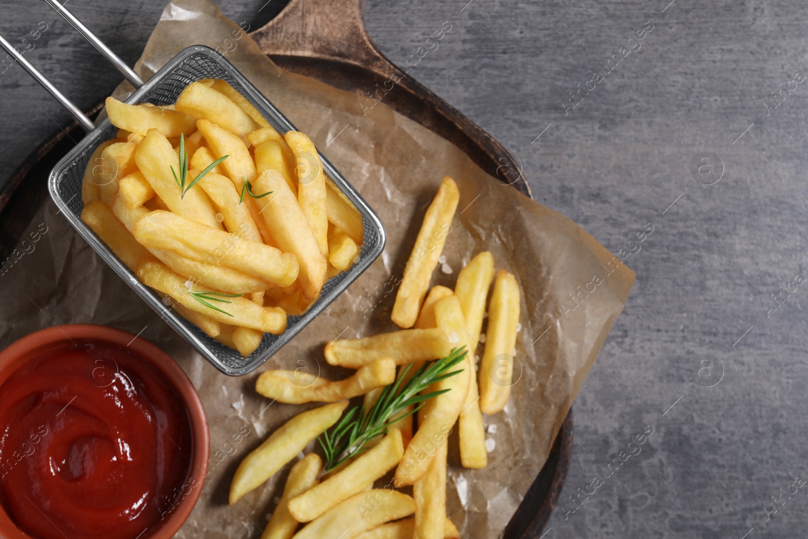 Photo of Tasty French fries, ketchup and rosemary on grey table, top view. Space for text