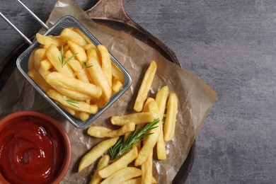 Photo of Tasty French fries, ketchup and rosemary on grey table, top view. Space for text