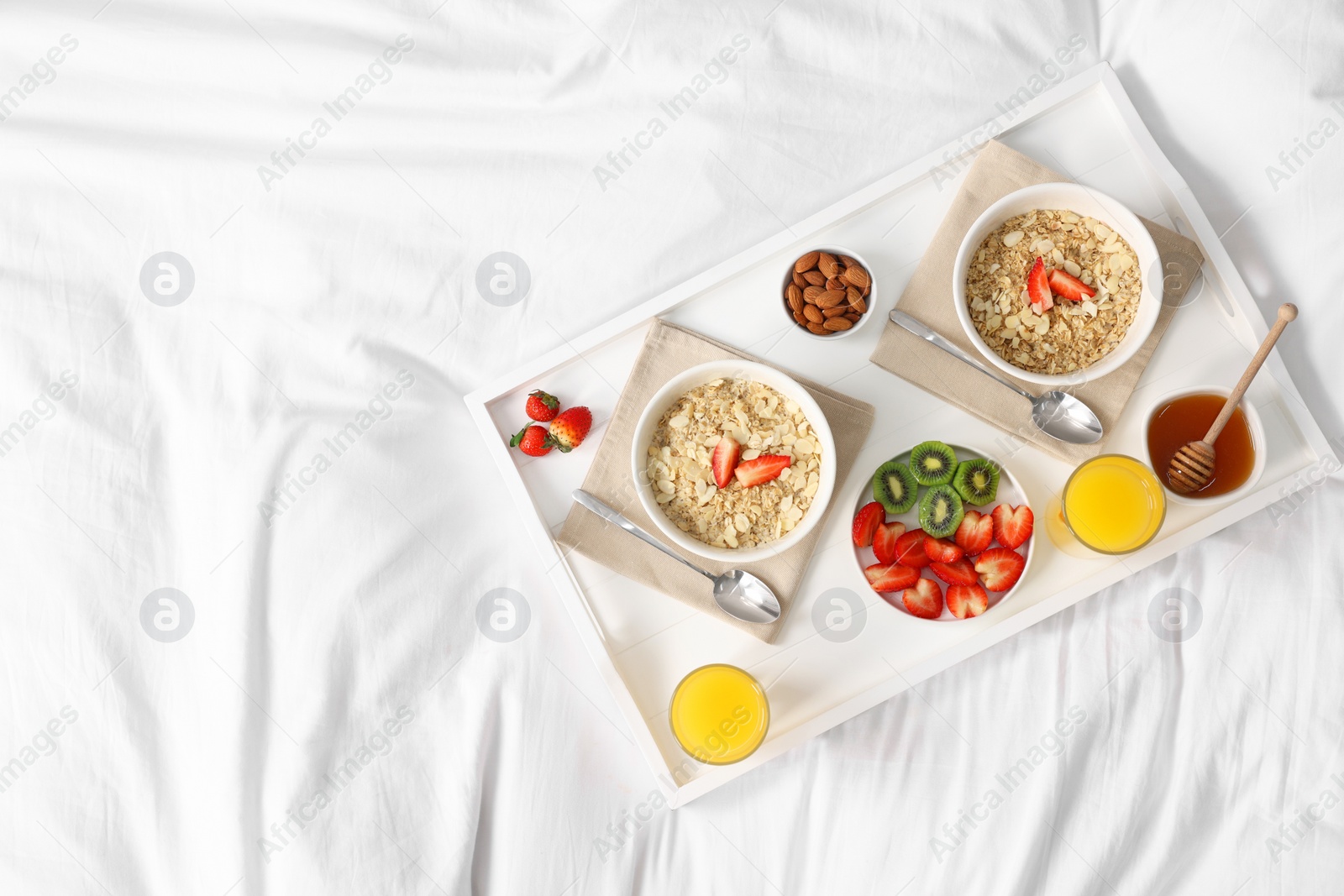 Tasty breakfast served in bed. Oatmeal, juice, fruits, almonds and honey on tray, top view. Space for text Photo of Tasty breakfast served in bed. Oatmeal, juice, fruits, almonds and honey on tray, top view. Space for text
