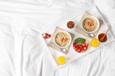 Photo of Tasty breakfast served in bed. Oatmeal, juice, fruits, almonds and honey on tray, top view. Space for text