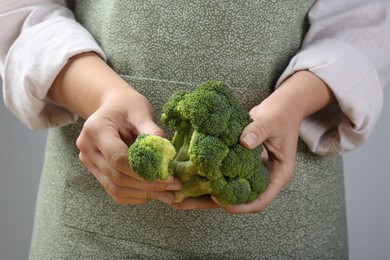 Woman with fresh broccoli on light grey background, closeup