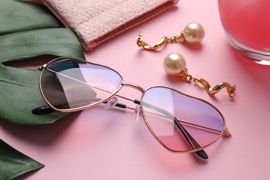 Photo of Stylish elegant heart shaped sunglasses and earrings on pink background, closeup