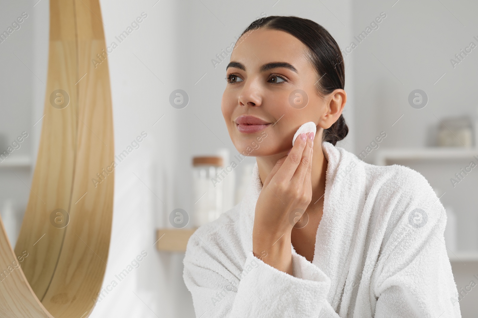 Photo of Beautiful woman removing makeup with cotton pad near mirror indoors, space for text