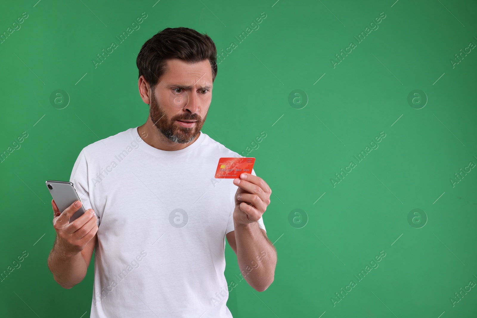 Photo of Emotional man with smartphone and credit card on green background, space for text. Be careful - fraud