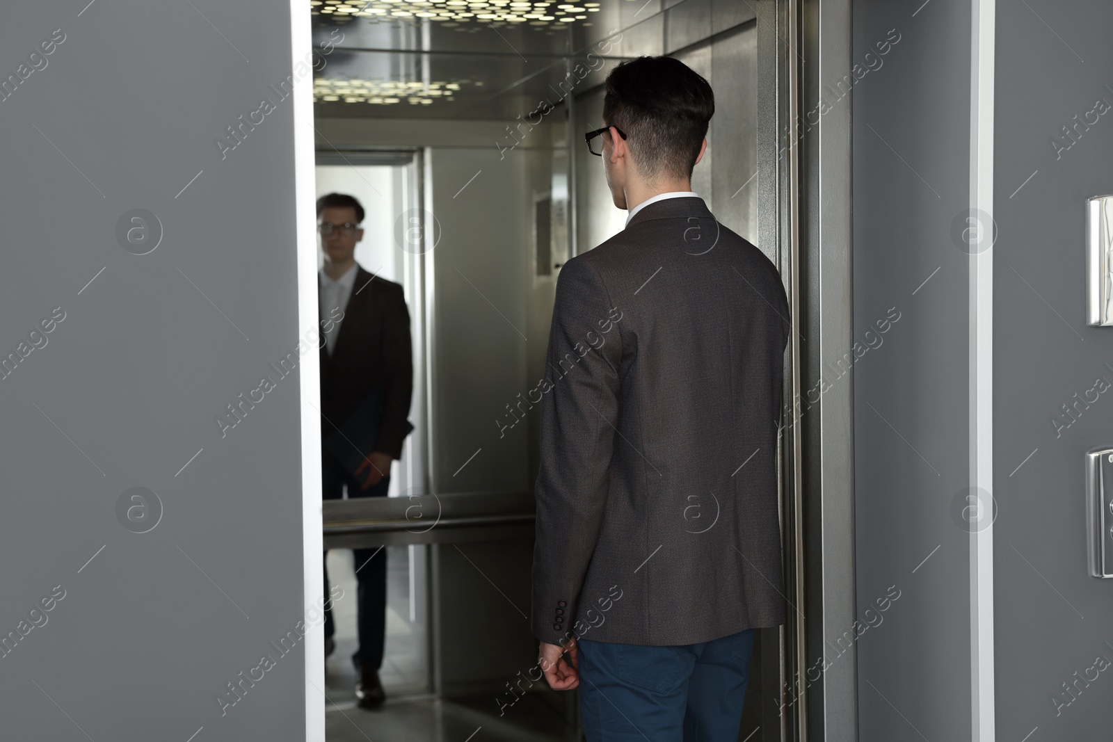 Photo of Young businessman entering modern elevator, back view