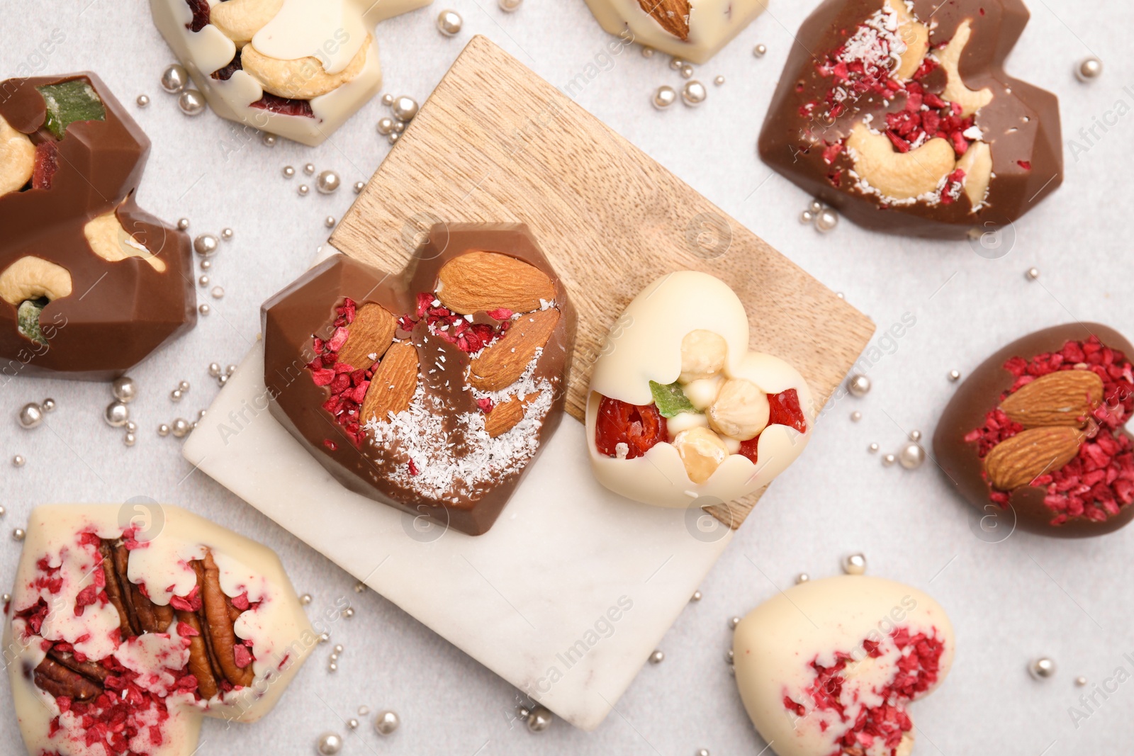 Photo of Tasty chocolate heart shaped candies with nuts on white table, flat lay