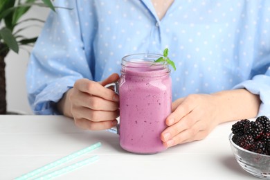 Photo of Woman with mason jar of delicious blackberry smoothie at white table indoors, closeup